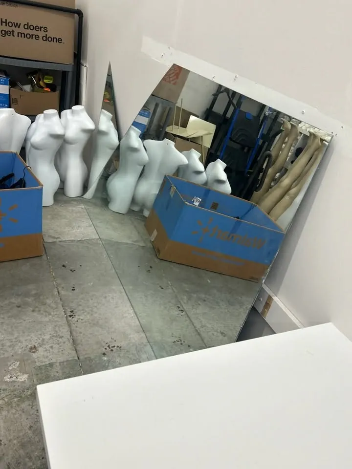 Large wall mirror propped against a stockroom wall, reflecting mannequin forms and boxes