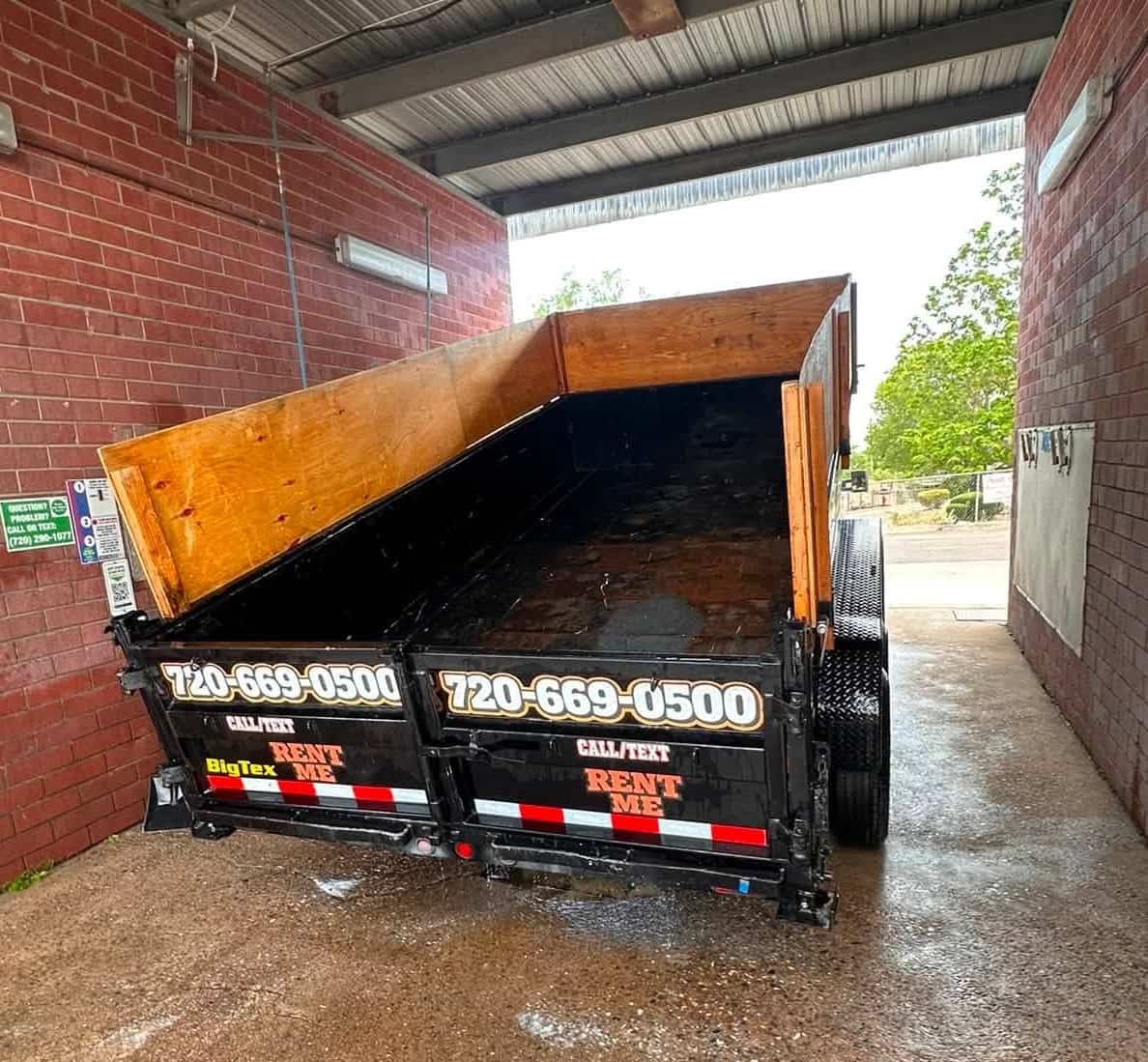 Empty black dump trailer with its bed tipped up and RENT ME lettering on the tailgate