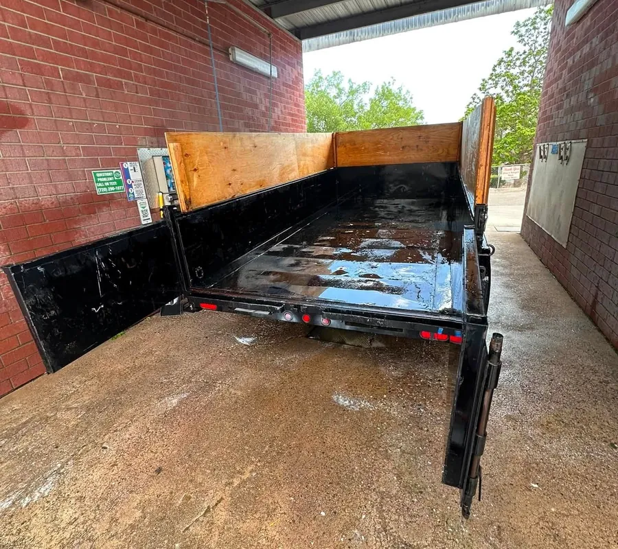 Empty black dump trailer with plywood sides, washed out in a wash bay