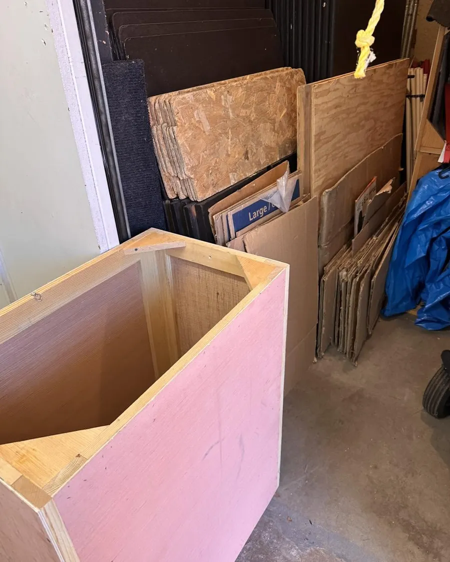 Plywood, chipboard, flattened cardboard and a pink wooden crate stacked in a storage unit in East Denver