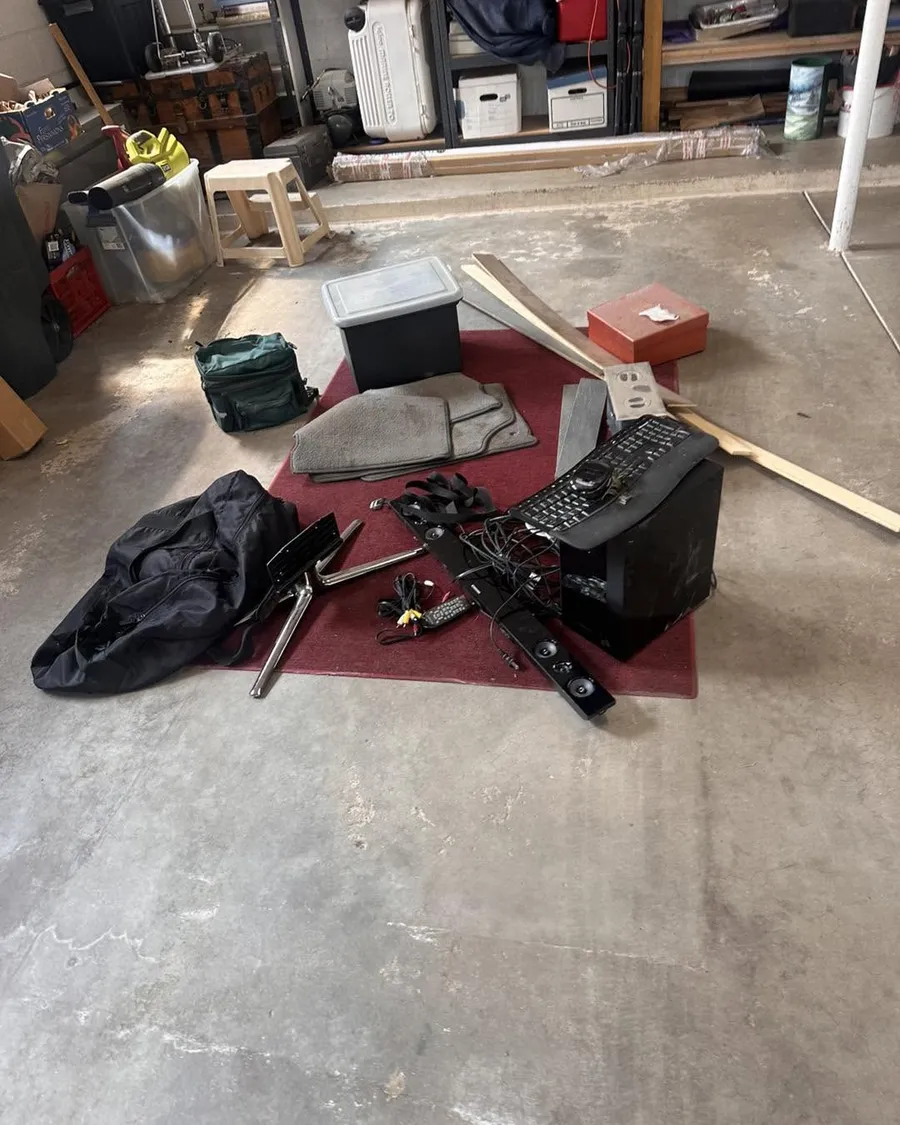 Old electronics, cords, a keyboard, car mats and bags laid out on a garage floor in Evergreen