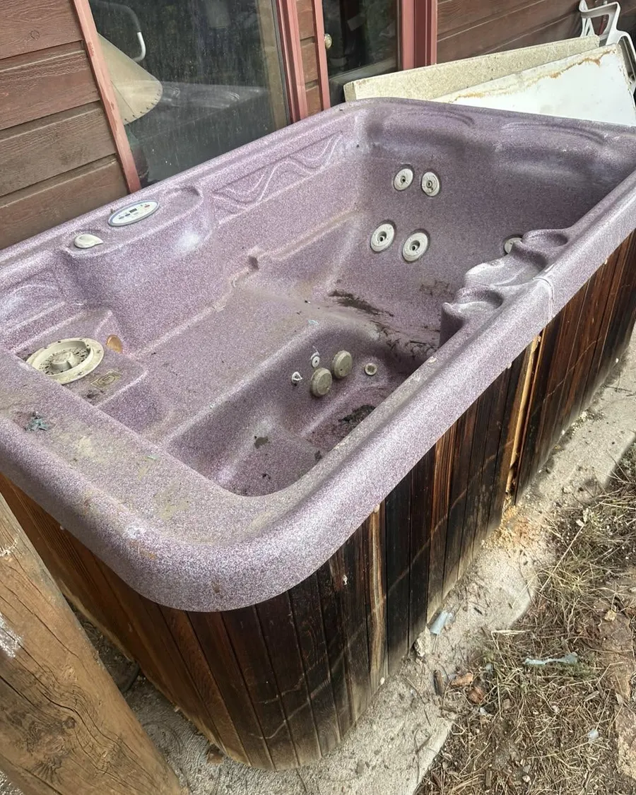 Old purple hot tub with wooden siding on a concrete pad beside a house in Evergreen