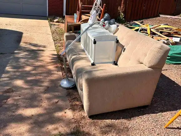 Before: old couch, storage boxes and household junk piled beside a garage