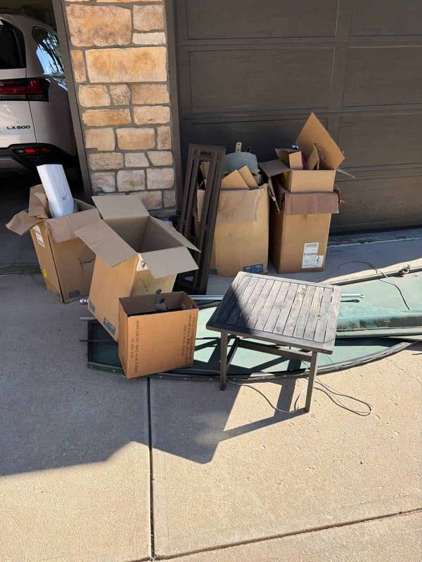 Flat pack boxes, a patio table and garden furniture stacked on a driveway ready for pickup