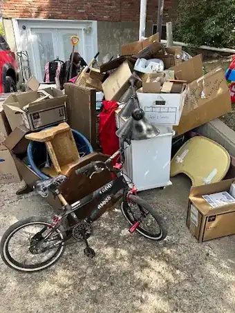Stack of cardboard boxes, a bike, a mini fridge and household clutter waiting for pickup