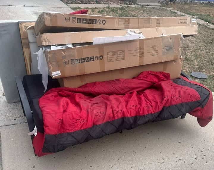 Futon with a red cover and flat-pack boxes waiting at the curb for a Lakewood pickup
