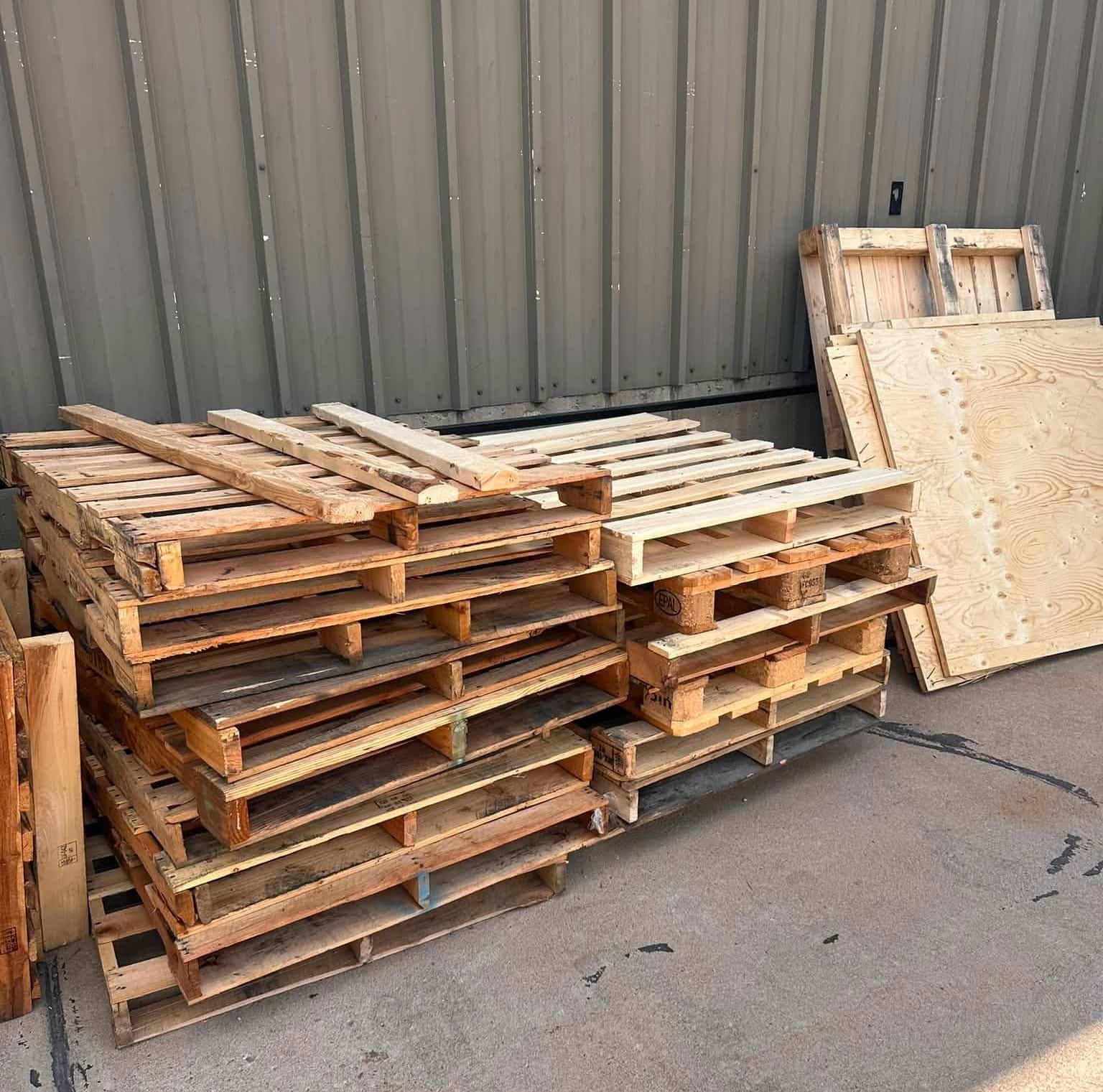 Stacks of wooden pallets and loose boards beside a commercial building before cleanup in North Lakewood