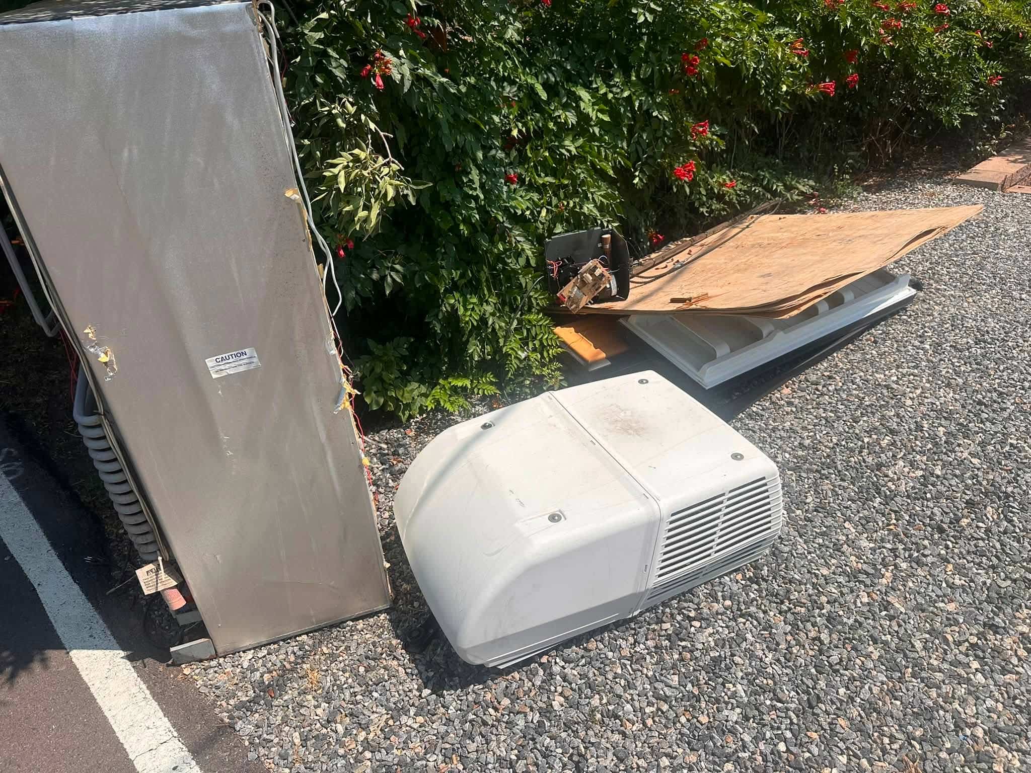 Old RV air conditioning equipment, a broken refrigerator panel and roofing scraps awaiting removal in West Lakewood
