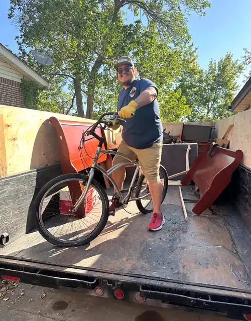Robert, owner of Bob's Round Up, standing on the trailer holding a bike he is hauling away