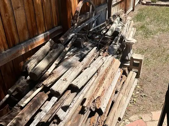 Before: a long pile of rotten timber and old fence boards stacked along a back fence