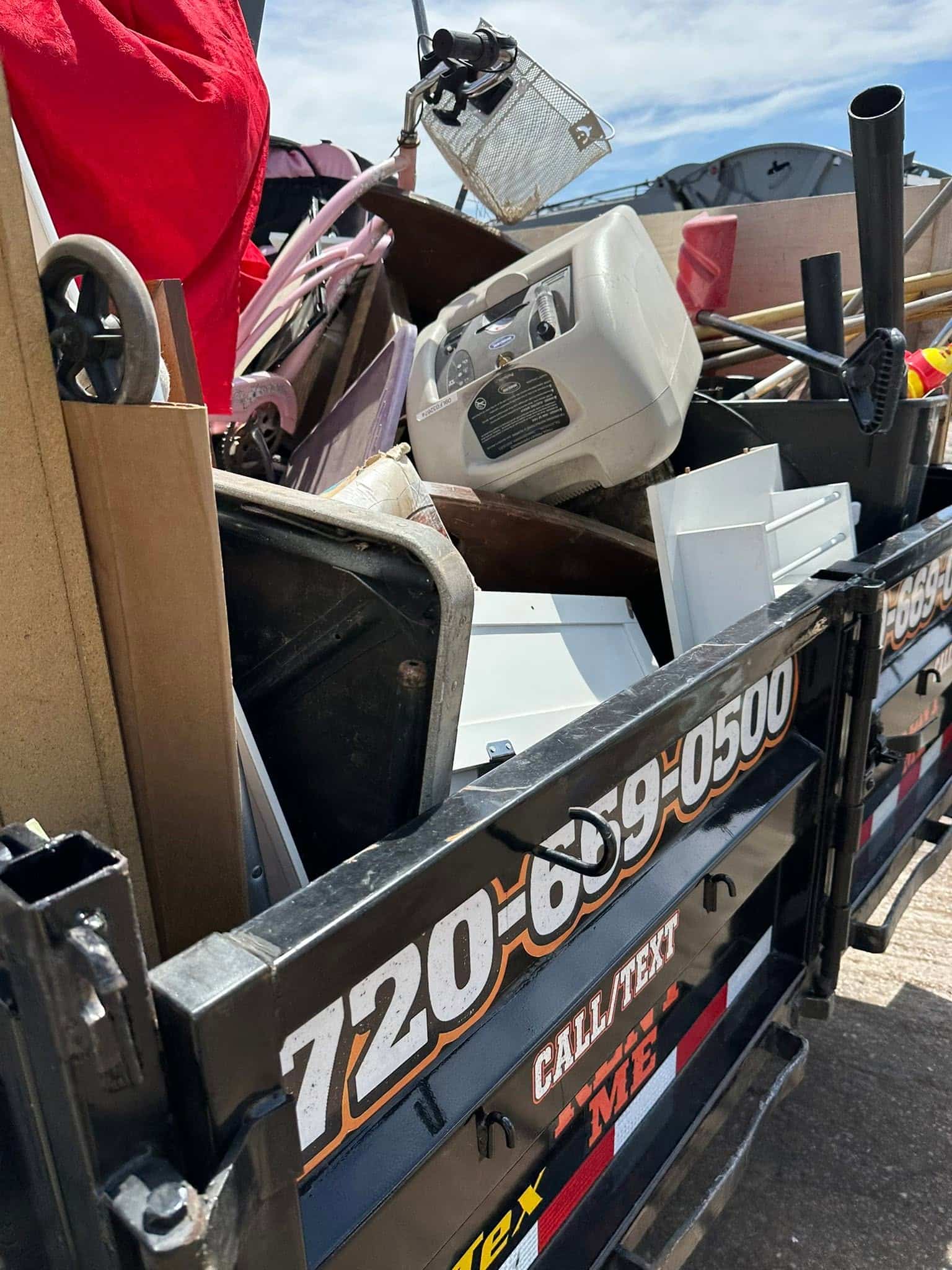Trailer loaded with a child's pink bike, furniture, white panels, and wood